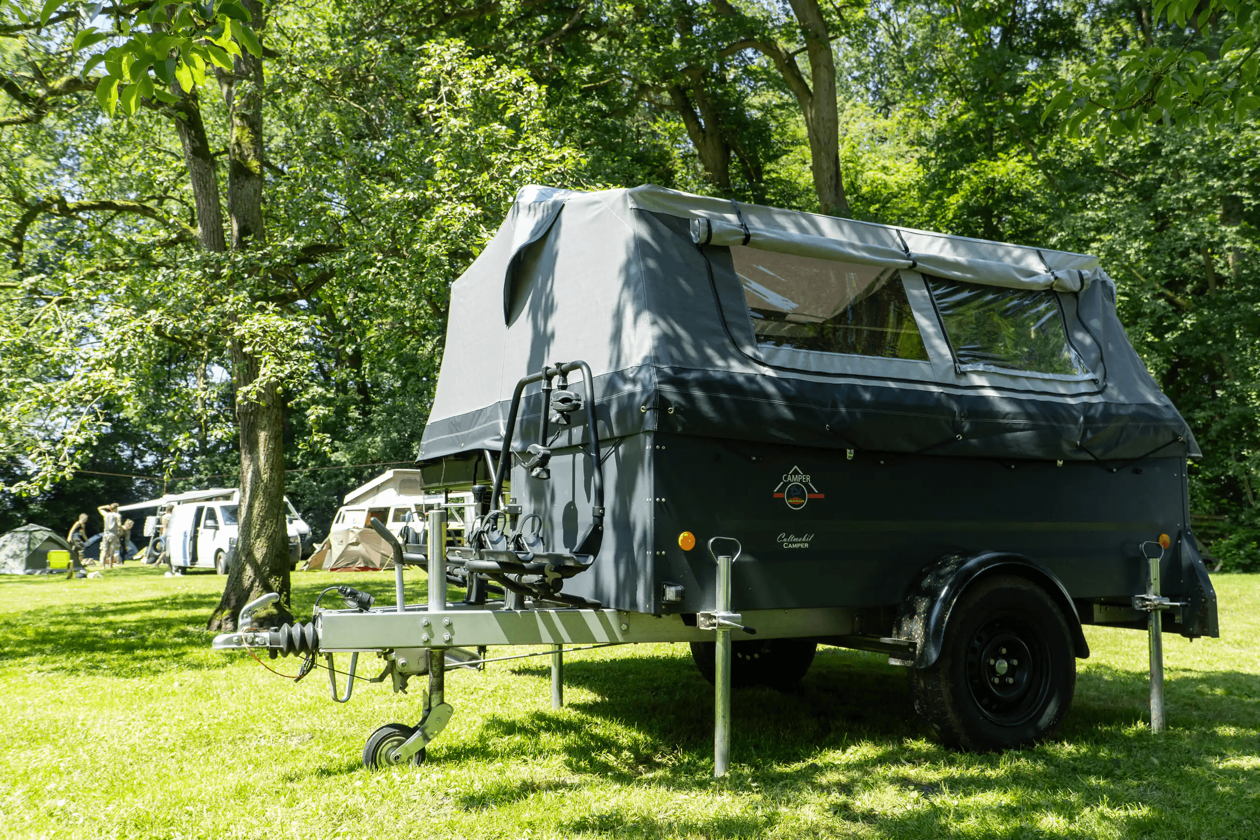 Cultmobil Klappcamper aufgebaut auf einem Campingplatz unter Bäumen, mit Fahrradträger auf der Deichsel