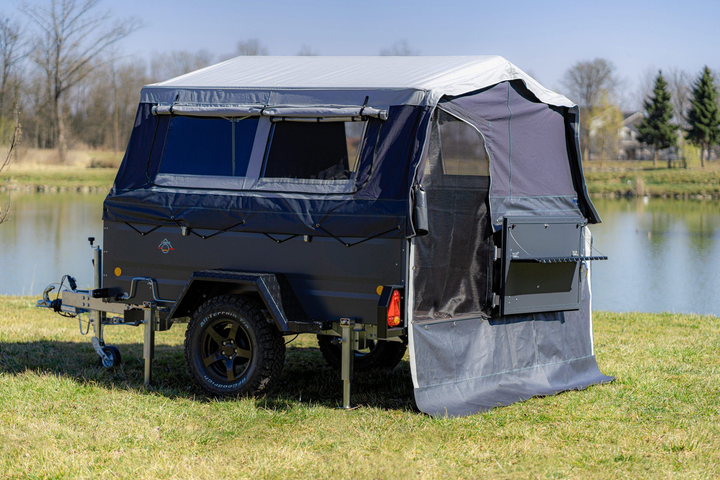 Campinganhänger mit aufgebautem Zelt auf einer Wiese am See