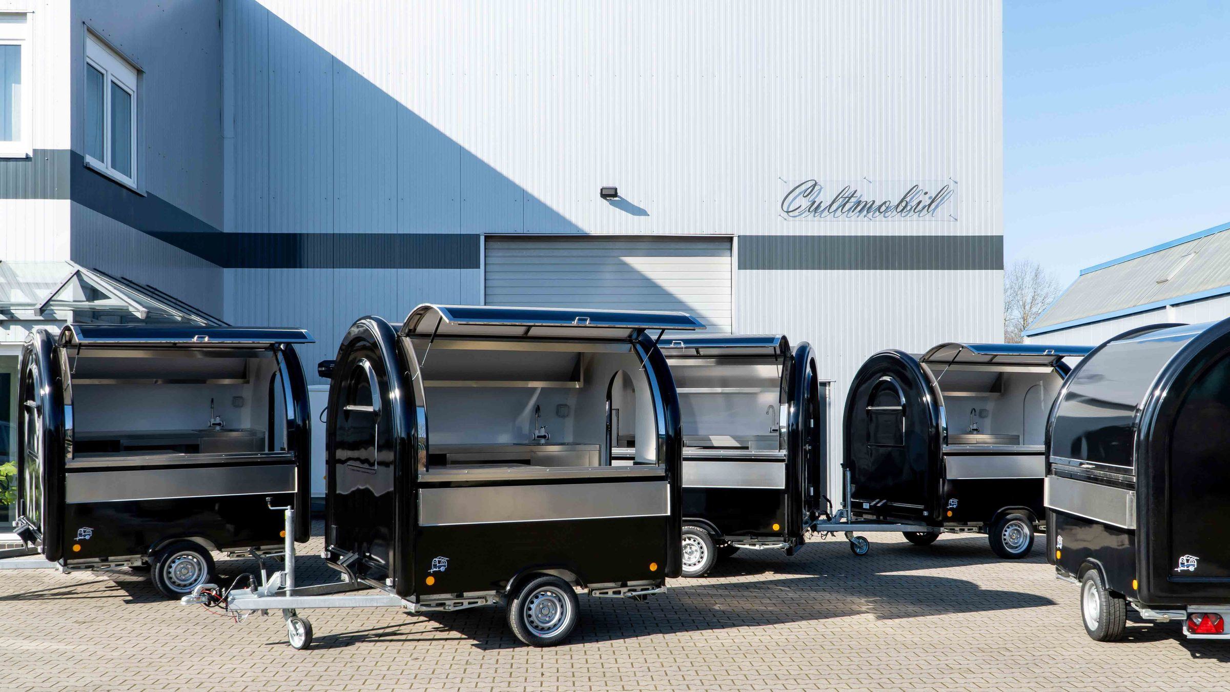 Mehrere schwarze Retro-Foodtrailer mit geöffneten Verkaufsklappen vor der Halle in Stuhr