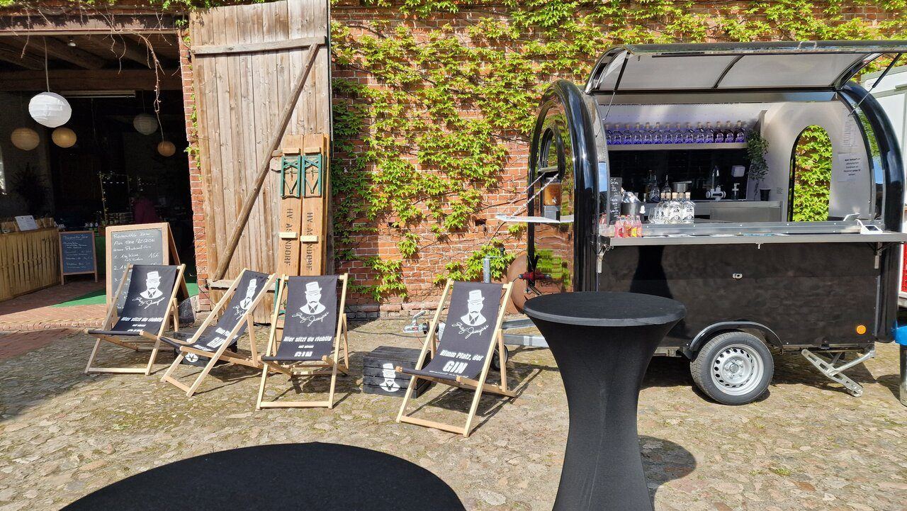 Schwarzer Retro-Foodtrailer als Cocktailbar mit Liegestühlen vor einer Scheune