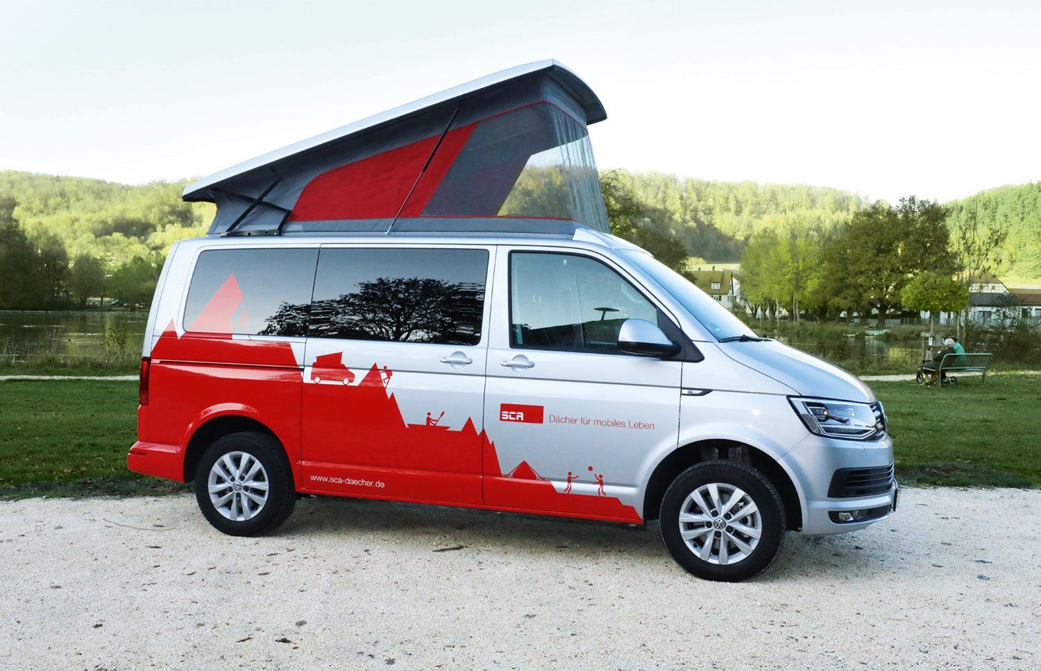 VW Camper mit rot-weißem Aufstelldach auf einem Campingplatz