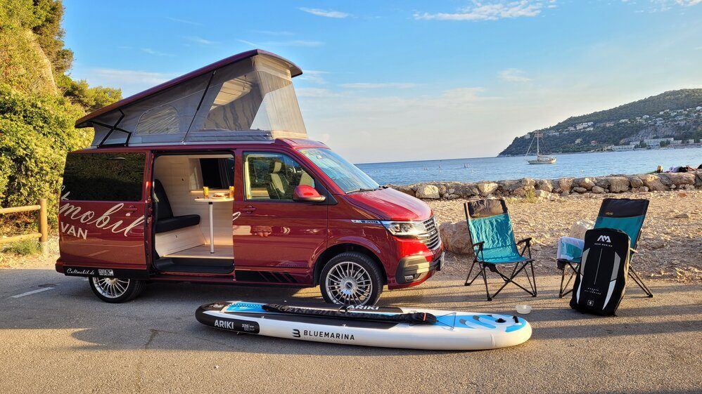 Cultmobil mit offenem Aufstelldach und SUP-Board am Strand